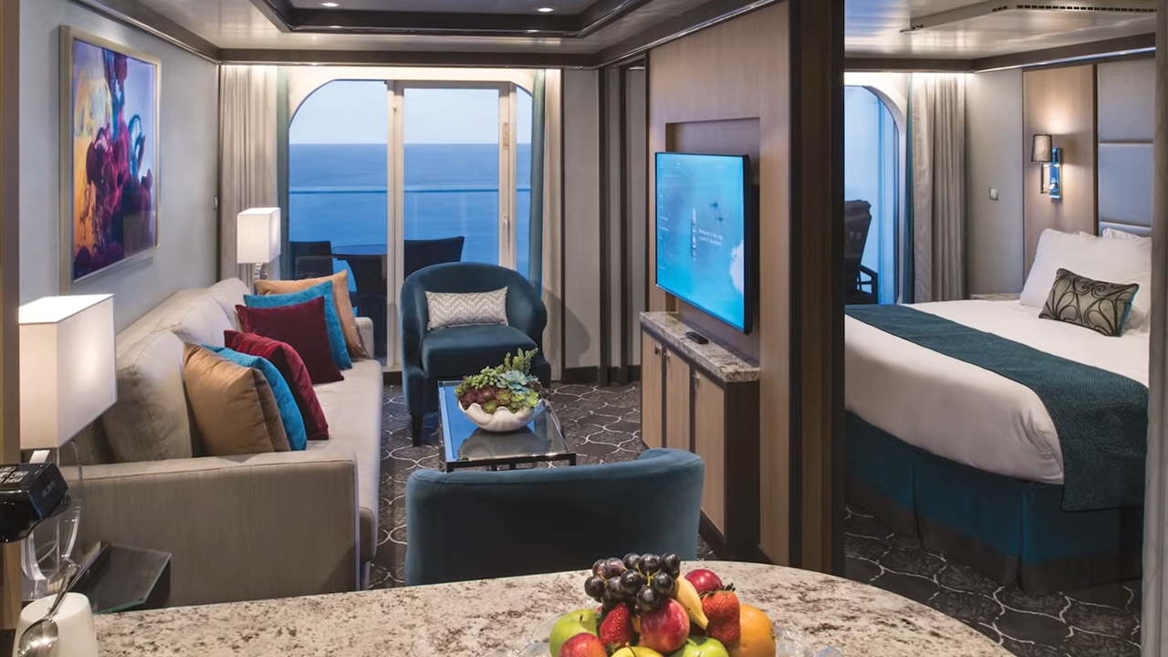 Modern Royal Caribbean Sky Class suite featuring an open-concept living area with a plush sofa, dining table, and a partitioned bedroom with ocean views.