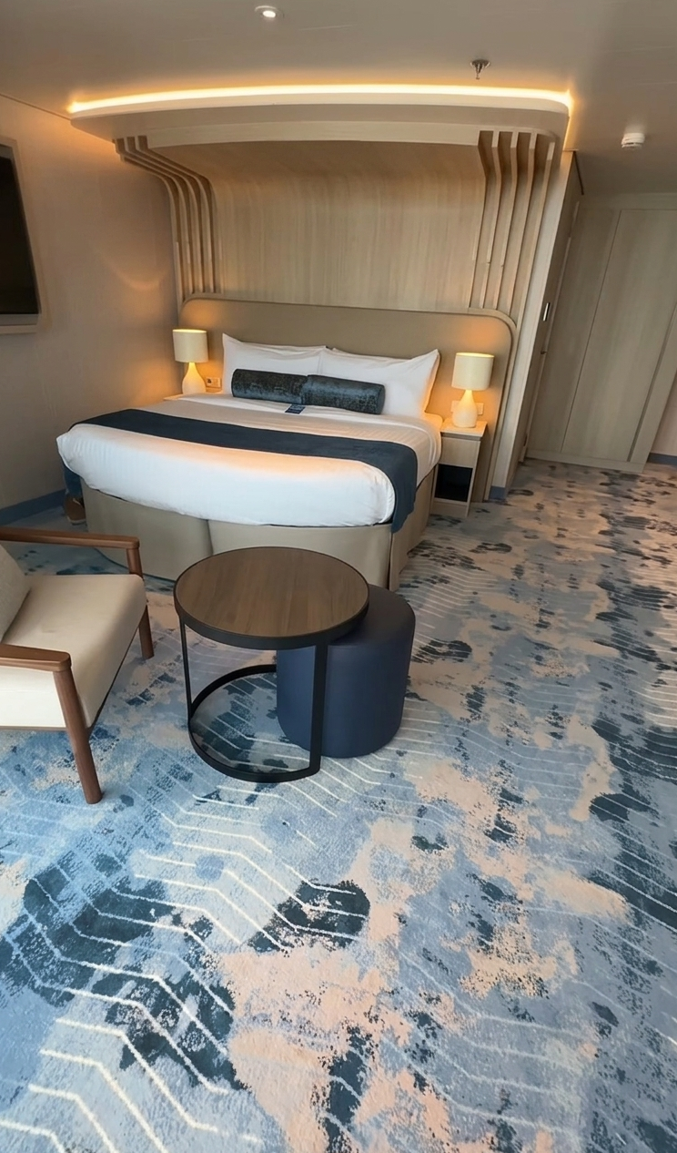 Modern Royal Caribbean Sky Class suite featuring an open-concept living area with a plush sofa, dining table, and a partitioned bedroom with ocean views.